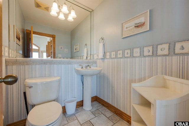 bathroom with wallpapered walls, toilet, a wainscoted wall, and a chandelier