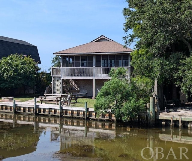 back of property with a sunroom, a water view, and stairs