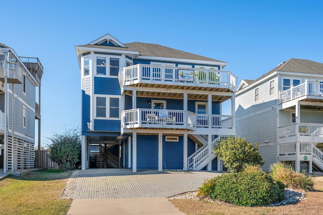 raised beach house with stairs, a carport, roof with shingles, and concrete driveway