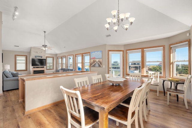 dining space with light wood finished floors, visible vents, lofted ceiling, ceiling fan, and a fireplace