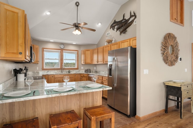 kitchen with stainless steel appliances, light countertops, a sink, a peninsula, and a kitchen bar