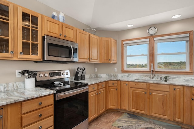 kitchen with appliances with stainless steel finishes, glass insert cabinets, a sink, and light stone countertops