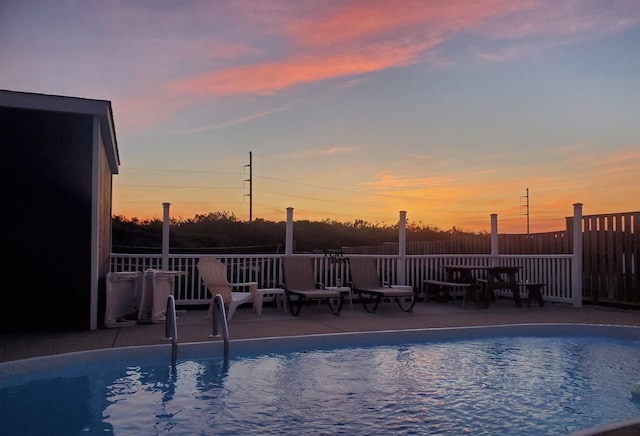 pool at dusk with a patio area, fence, and a fenced in pool