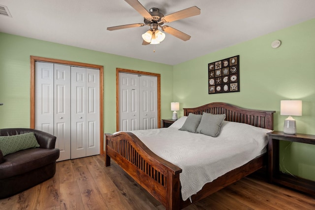 bedroom featuring visible vents, a ceiling fan, multiple closets, and wood finished floors