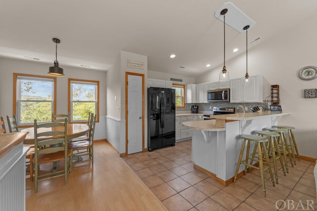 kitchen featuring stainless steel appliances, hanging light fixtures, white cabinets, a peninsula, and a kitchen bar