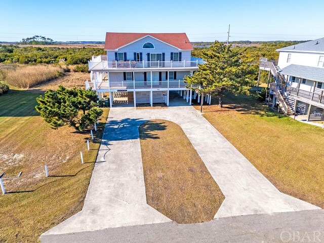 raised beach house with concrete driveway, a balcony, stairway, covered porch, and a carport