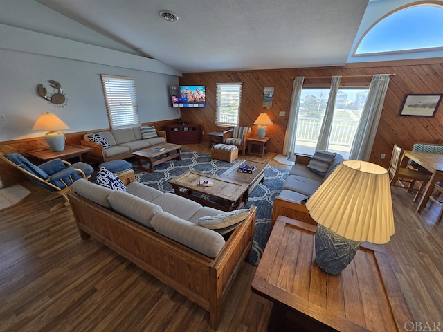 living area with dark wood-type flooring, lofted ceiling, visible vents, and wooden walls