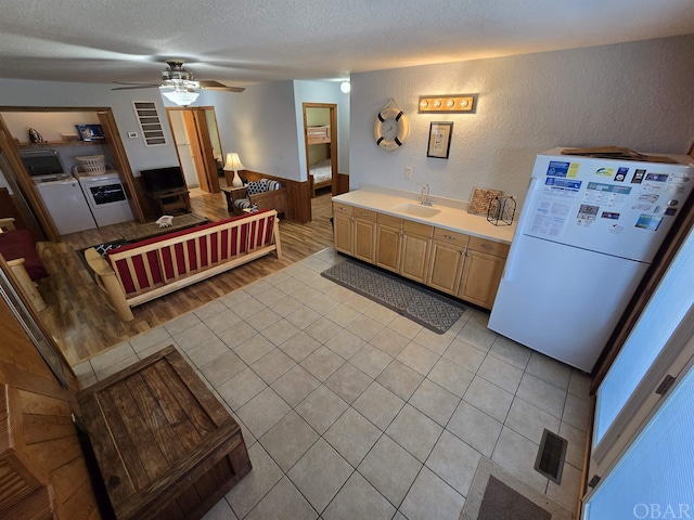 kitchen with freestanding refrigerator, light countertops, a textured ceiling, separate washer and dryer, and a sink