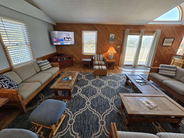 living room with lofted ceiling, a healthy amount of sunlight, wooden walls, and wood finished floors