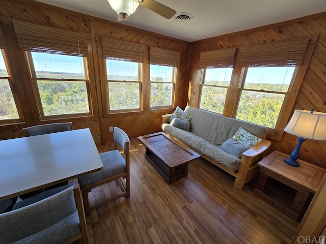 living room featuring ceiling fan, wood walls, wood finished floors, and visible vents