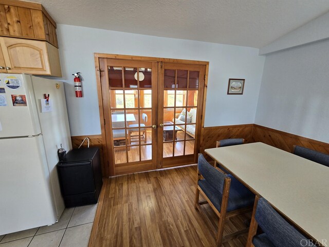 dining space featuring french doors, a wainscoted wall, wood walls, and a textured ceiling