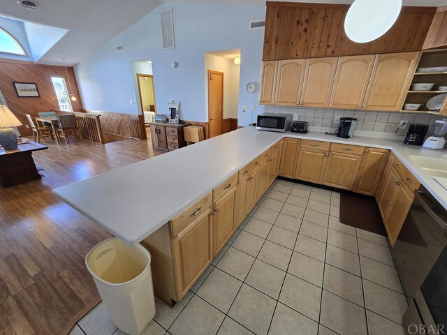 kitchen with vaulted ceiling with skylight, light countertops, stainless steel microwave, and a peninsula