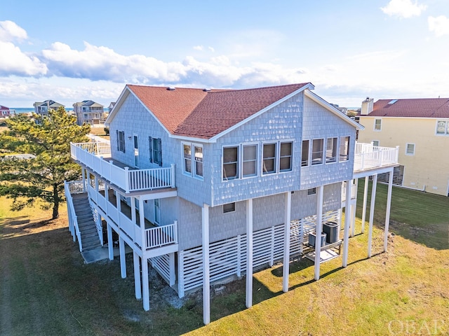 rear view of house with cooling unit, a balcony, a yard, stairway, and roof with shingles