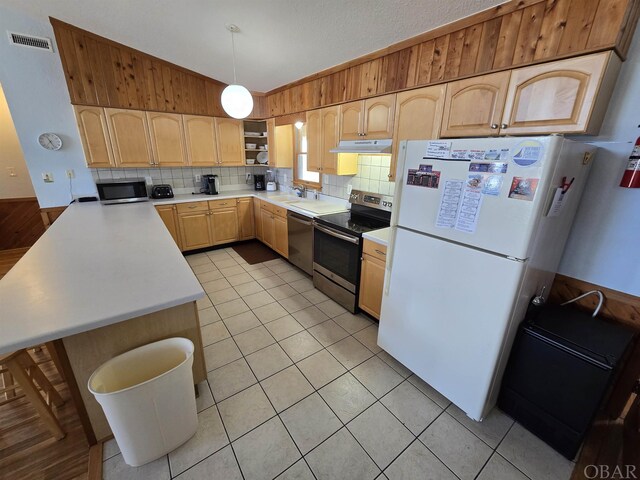 kitchen with stainless steel appliances, light countertops, light brown cabinetry, under cabinet range hood, and pendant lighting