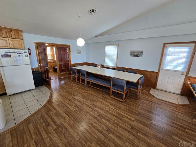 dining room featuring a wainscoted wall, vaulted ceiling, light wood-type flooring, and visible vents