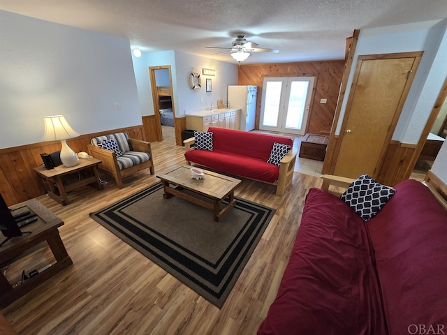 living area with a textured ceiling, light wood finished floors, wainscoting, and wooden walls