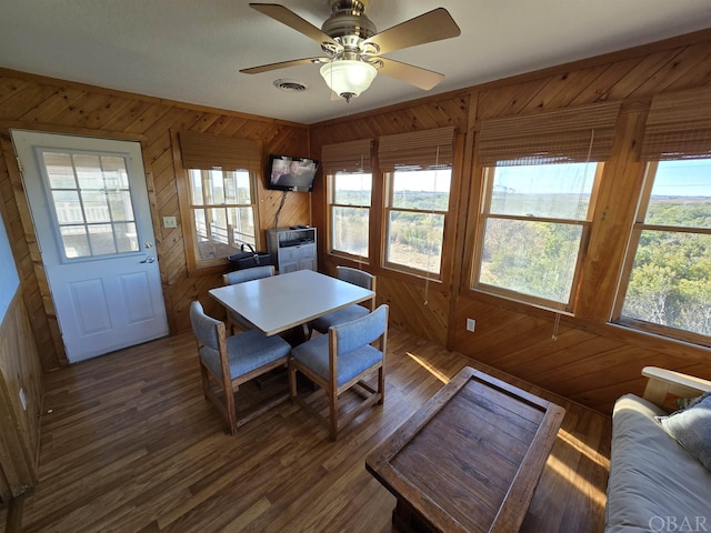 dining space featuring wood walls, a ceiling fan, visible vents, and dark wood-type flooring