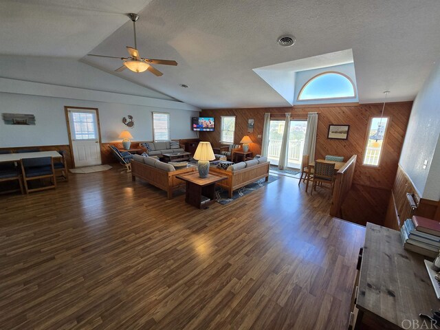 living area with dark wood-style floors, wood walls, lofted ceiling, and visible vents