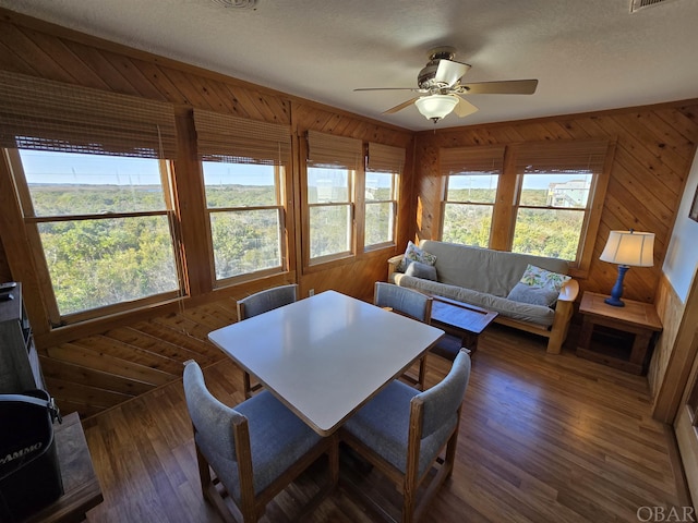 dining room with dark wood-style flooring, plenty of natural light, wood walls, and ceiling fan