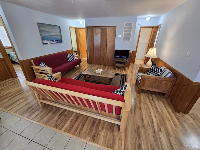 living area featuring light wood finished floors, wood walls, and wainscoting