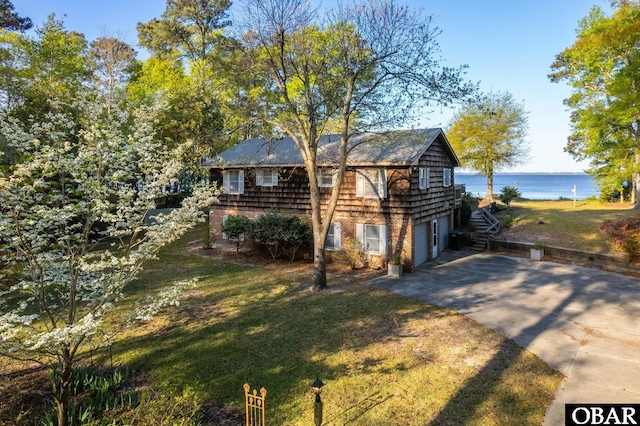 view of front of house featuring concrete driveway, a front yard, a water view, and a garage