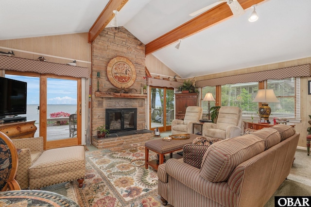 carpeted living area with wood walls, lofted ceiling with beams, and a stone fireplace