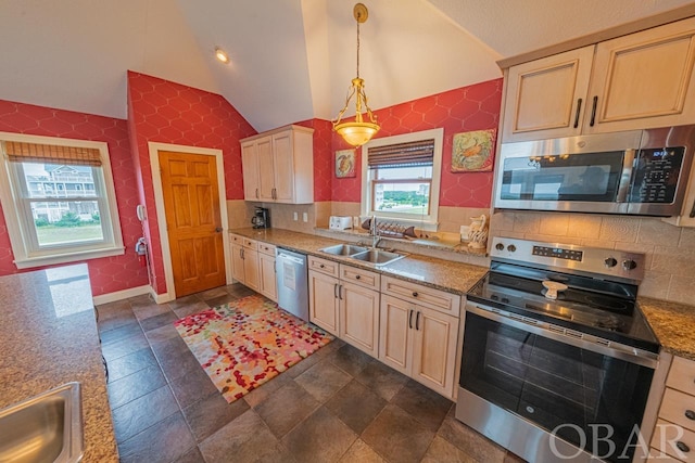 kitchen featuring lofted ceiling, appliances with stainless steel finishes, decorative light fixtures, stone counters, and a sink