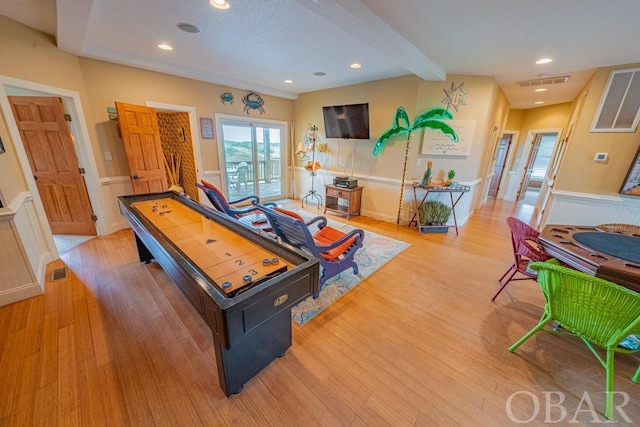 rec room featuring light wood-type flooring, a wainscoted wall, visible vents, and beam ceiling