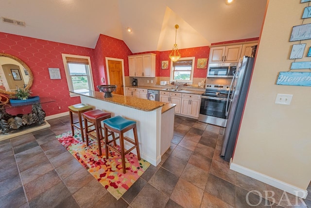 kitchen featuring a sink, a kitchen island, hanging light fixtures, appliances with stainless steel finishes, and a kitchen bar