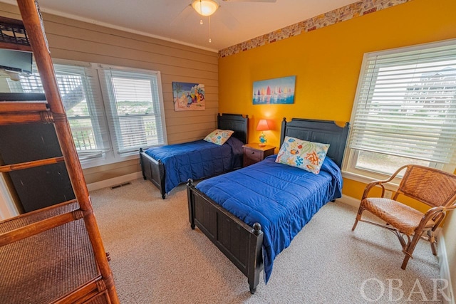 carpeted bedroom with wooden walls, baseboards, multiple windows, and visible vents