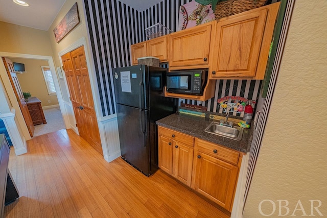 kitchen with dark countertops, black appliances, a sink, and light wood-style floors