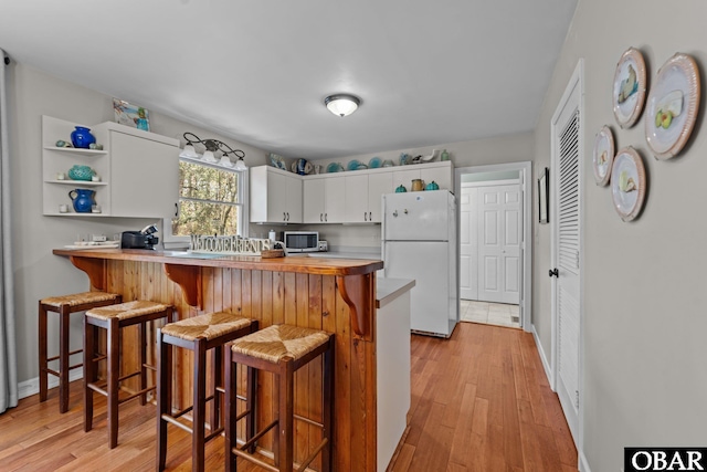 kitchen featuring light wood-type flooring, white cabinetry, a breakfast bar, and freestanding refrigerator