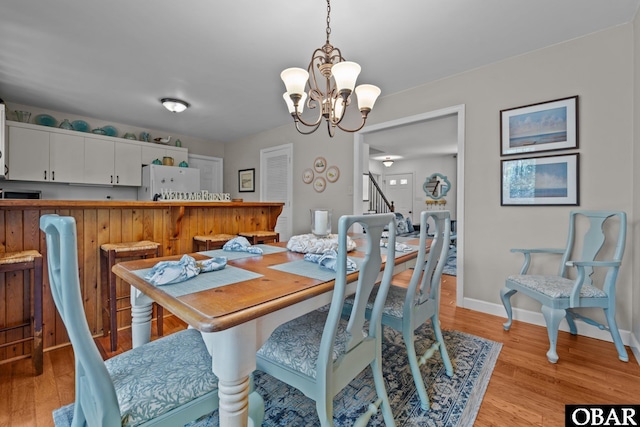 dining area with light wood finished floors, a chandelier, stairs, and baseboards