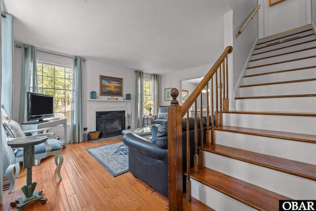 living room with light wood-type flooring, a fireplace with flush hearth, and stairway