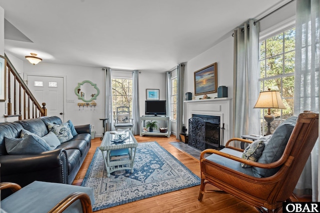 living area featuring a fireplace with flush hearth, stairs, baseboards, and wood finished floors