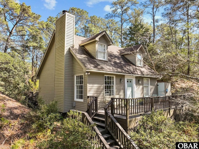 cape cod-style house featuring a deck, stairway, a shingled roof, and a chimney