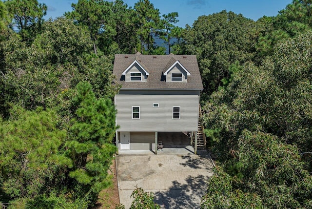 view of front of house with stairs, concrete driveway, a carport, and a forest view