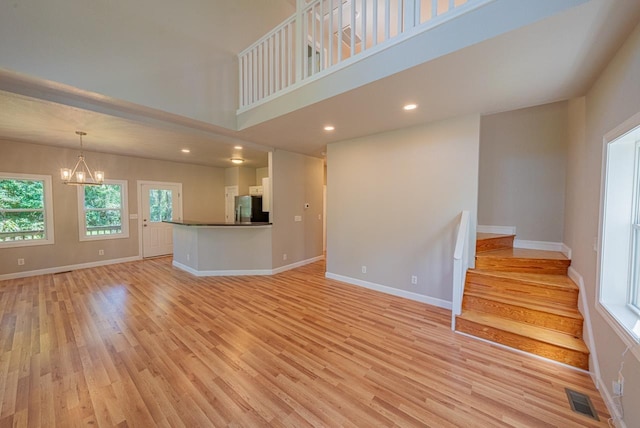 unfurnished living room with baseboards, light wood-style flooring, visible vents, and an inviting chandelier