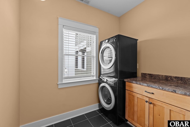 laundry area with cabinet space, visible vents, baseboards, dark tile patterned flooring, and stacked washer and clothes dryer