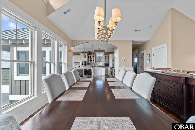 dining space with dark wood-type flooring, lofted ceiling, visible vents, and a notable chandelier