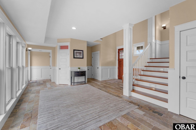 interior space featuring a wainscoted wall, a decorative wall, ornate columns, and stairs