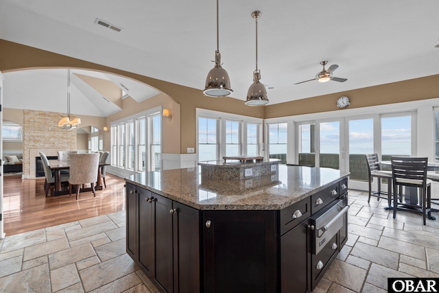 kitchen featuring light stone counters, decorative light fixtures, stone tile flooring, visible vents, and a kitchen island