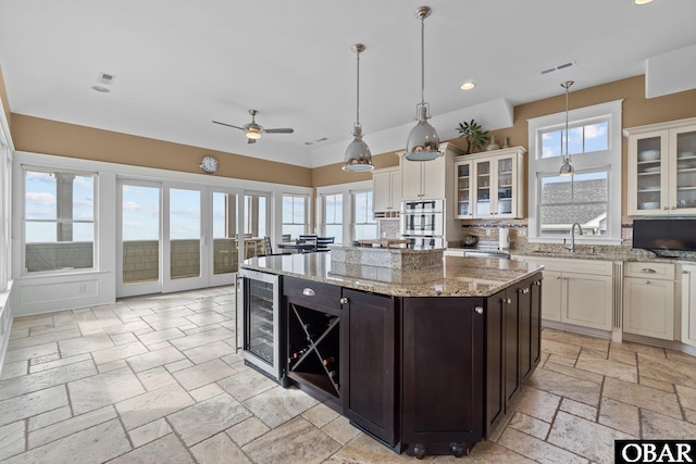 kitchen featuring dark brown cabinetry, stone tile floors, visible vents, wine cooler, and glass insert cabinets