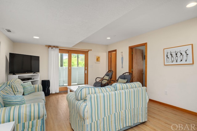 living room featuring a textured ceiling, light wood-style flooring, recessed lighting, visible vents, and baseboards