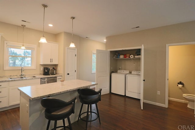 kitchen featuring light stone counters, a sink, white cabinets, stainless steel dishwasher, and a center island