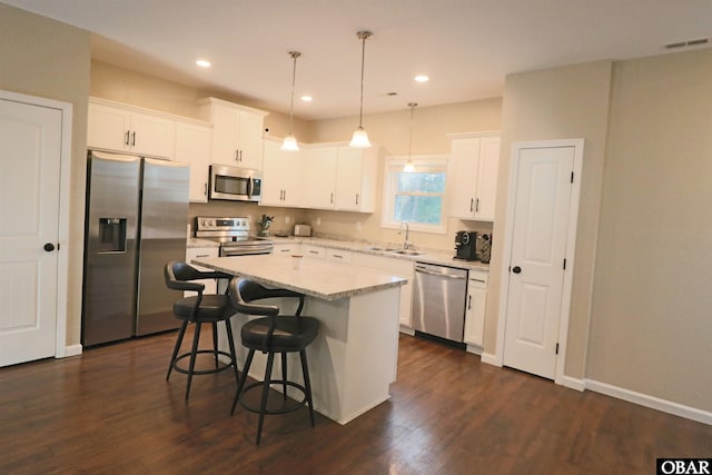 kitchen featuring appliances with stainless steel finishes, white cabinets, a kitchen island, and decorative light fixtures