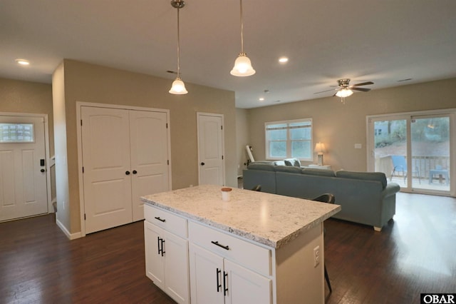 kitchen featuring white cabinets, a kitchen island, light stone counters, open floor plan, and hanging light fixtures