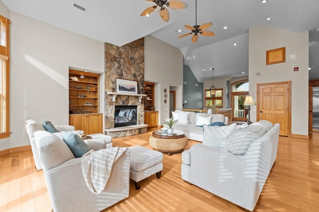 living room featuring high vaulted ceiling, built in shelves, a fireplace, visible vents, and light wood-type flooring