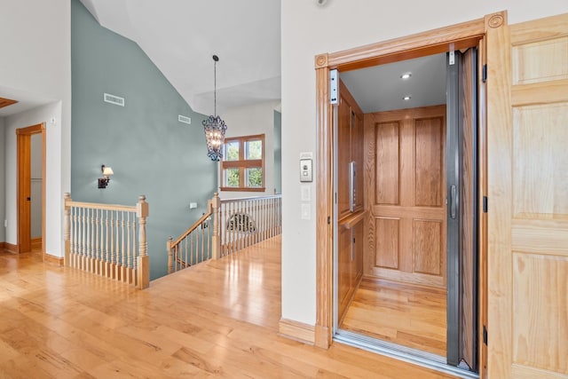 corridor featuring elevator, visible vents, wood finished floors, and an upstairs landing