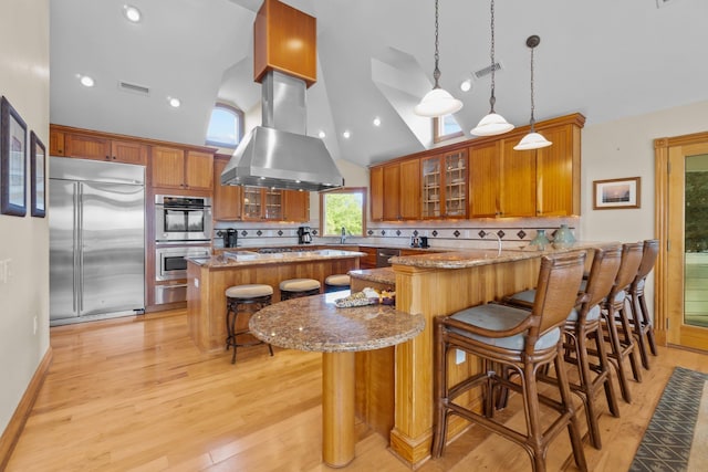 kitchen featuring stainless steel appliances, a kitchen island, light stone countertops, a kitchen bar, and glass insert cabinets